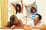 Young Family Having Pillow Fight In Bedroom