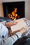 Detail Of Senior Woman Reading Book By Fire At Home