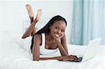 Happy woman lying on her belly using a laptop in her bedroom