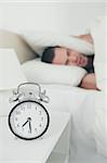 Portrait of a man covering his ears with a pillow while his alarm clock is ringing