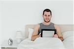 Cute man using a tablet computer in his bedroom