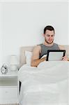 Portrait of an attractive man using a tablet computer in his bedroom