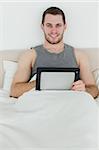 Portrait of a happy man using a tablet computer in his bedroom