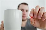 Man showing a pill and and a mug in his bedroom