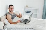 Happy man purchasing online with thumb up in his bedroom