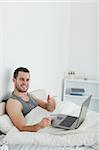 Portrait of a man purchasing online with thumb up in his bedroom