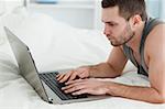 Young man using a laptop while lying on his belly in his bedroom