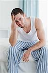 Portrait of a depressed man sitting on his bed while looking at the camera