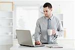 Businessman using a laptop while drinking coffee in his kitchen