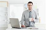 Businessman using a notebook while drinking coffee in his kitchen