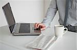 Businessman using a laptop with a cup of tea and a newspaper in his kitchen