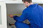 Focused repair man measuring something in a kitchen