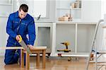 Young handyman cutting a wooden board in a kitchen