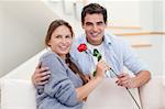 Young man offering a rose to his wife in their living room