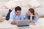 Smiling couple surfing on the internet while lying on a carpet