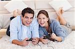 Delighted couple playing video games while lying on a carpet