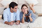 Lovely couple playing video games while lying on a carpet