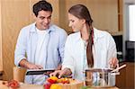 Charming couple using a tablet computer to cook in their kitchen