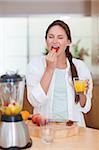 Portrait of a cute woman eating a fresh strawberry in her kitchen