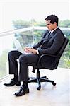 Portrait of a businessman sitting on an armchair working with a laptop in his office