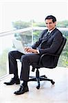 Portrait of a young businessman sitting on an armchair working with a laptop in his office