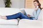 Young smiling woman on the sofa booking a flight online