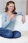 Smiling young female surfing the web with her smartphone on the sofa