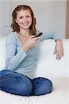 Smiling young woman on the couch typing text message