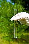 hand holding test tube with clear water outdoors