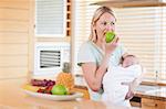 Young woman biting into apple with baby on her arms
