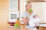 Young woman chewing on apple while holding baby on her arms
