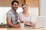 Smiling couple using a notebook while having coffee in their kitchen