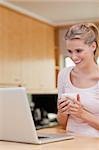 Portrait of a young woman using a laptop while drinking coffee in her kitchen