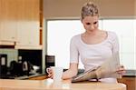 Young woman reading the news while having tea in her kitchen