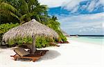 Beautiful tropical paradise in Maldives with coco palms hanging over the white and turquoise sea. Parasol is in the front.