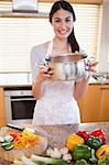 Portrait of a woman showing a sauce pan in her kitchen