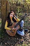 Beautiful brunette guitar player girl in the autumn forest