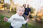 Cute Young Boy Walking in the park as Parents Look On From Behind.