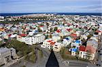 View over the city of Reykjavik seen from the top of the tower of Hallgrimur church. A nice view with the shadow of the tower top seen at the street below. Colorful houses with the ocean and blue sky in the background.