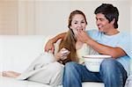 Happy couple watching television while eating popcorn in their living room