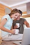 Portrait of a young couple having tea while using a laptop in their kitchen