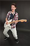 Photo of a teenage male playing a white electric guitar and making a rock and roll face.