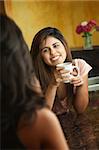 Smiling young Hispanic lady enjoys coffeewith friend