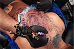 Tattooist with black gloves creates a design on woman's back
