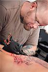 Caucasian tattoo artist inks a design on customer's back