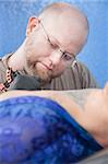 Bald Caucasian tattoo artist makes a design on client's back