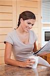 Smiling young woman reading newspaper in the kitchen