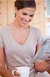 Smiling young woman reading newspaper while having coffee