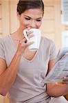 Young woman taking a sip of coffee while reading newspaper