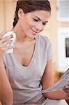 Young woman reading newspaper while holding cup of tea
